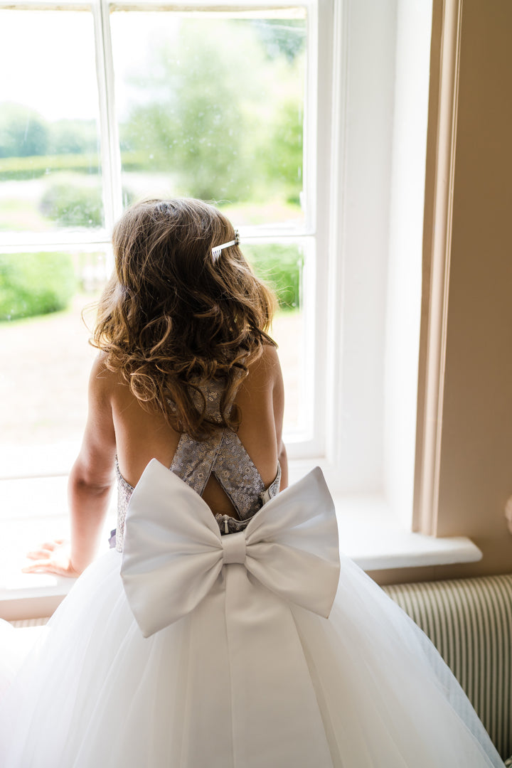 The City Shimmer childrens dress with Silver Sequin Bodice and adjustable straps. A line white tulle skirt and oversized white satin bow and tails at the back. This dress is perfect for Flower girls, little bridesmaids, pageants, wedding guest, birthday parties or any special occasion in your social calendar.