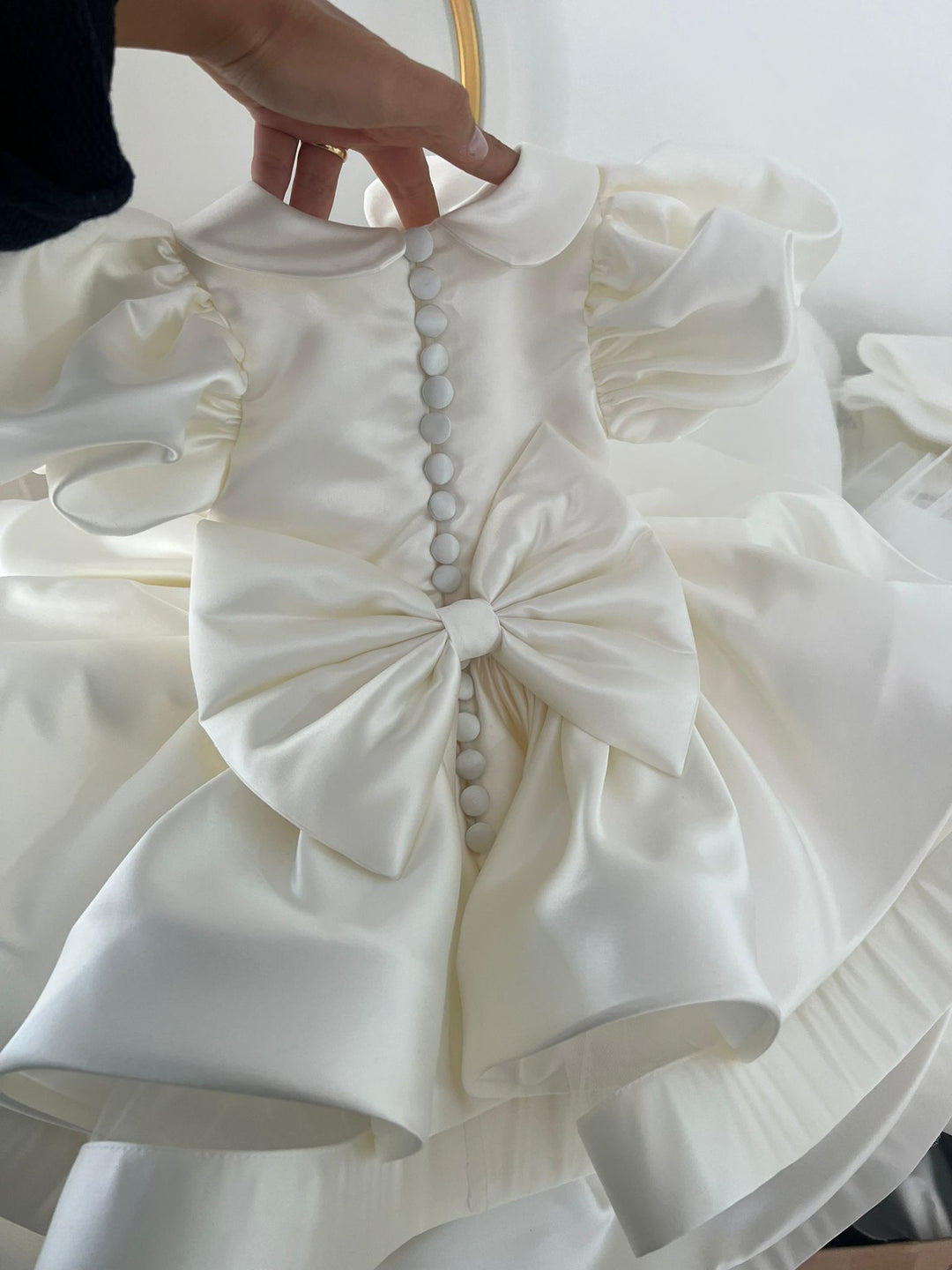 The timeless Valetina Dress in Ivory Satin. Timeless design with satin covered buttons at the back and oversized Little London lady Satin Bow. This design has a delicate Puff Sleeve but also the option of a long satin sleeve. Perfect as a Christening, Baptism, Naming Ceromony, photoshoot Dress. The full and elegant skirt makes this design so playfull. Satin Bloomers and Knickers are also available to purchase.