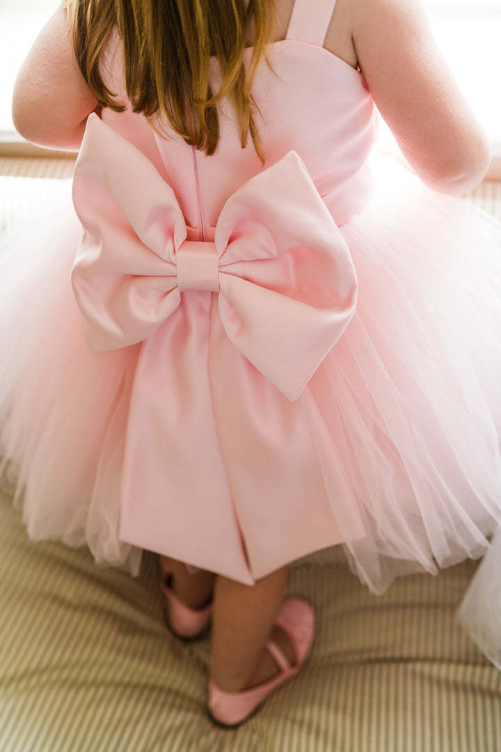 Little girl in baby pink tutu dress with large satin bow. Pink princess shoes. Ideal Flower girl or Party dress.  Can also come with a detachable train.