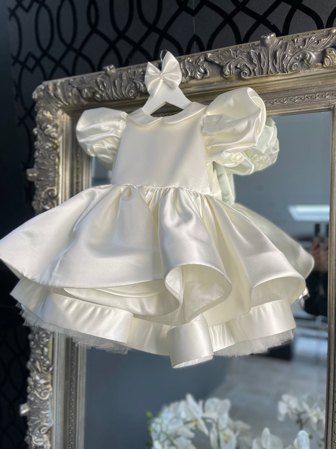 The perfect Flower Girl  dress, the Valentina, The timeless Valentina Dress in Ivory Bridal Satin. Timeless design with satin covered buttons at the back and oversized Little London lady Satin Bow. This design has a delicate Puff Sleeve but also the option of a long satin sleeve. Perfect as a Christening, Baptism, Naming Ceromony, photoshoot Dress. The full and elegant skirt makes this design so playful.  Luxury Bridal Satin Bloomers and Knickers are also available to purchase. Made by Artisans.