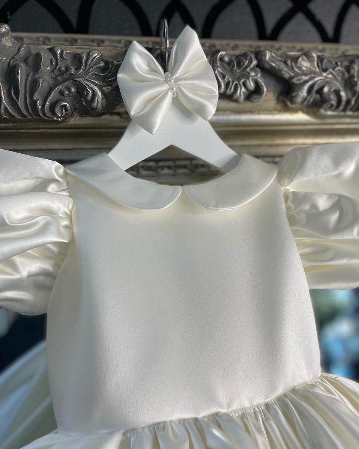 The timeless Valetina Dress in Ivory Satin. Timeless design with satin covered buttons at the back and oversized Little London lady Satin Signature Bow. This design has a delicate Puff Sleeve but also the option of a long satin sleeve. Perfect as a Christening, Baptism, Naming Ceromony, photoshoot Dress. Also comes with Satin hair clip.